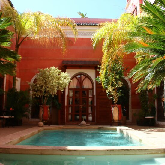 Binnenplaats met zwembad en palmen in een traditionele riad in Marrakech