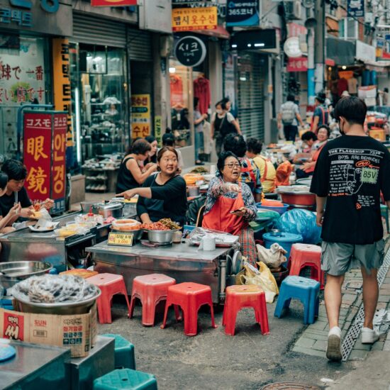Druk marktstraatje met eetkraampjes en kleurrijke krukjes in Busan