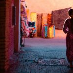 Vrouw wandelt door een poort naar een kleurrijk tapijtwinkeltje in de medina van Marrakech