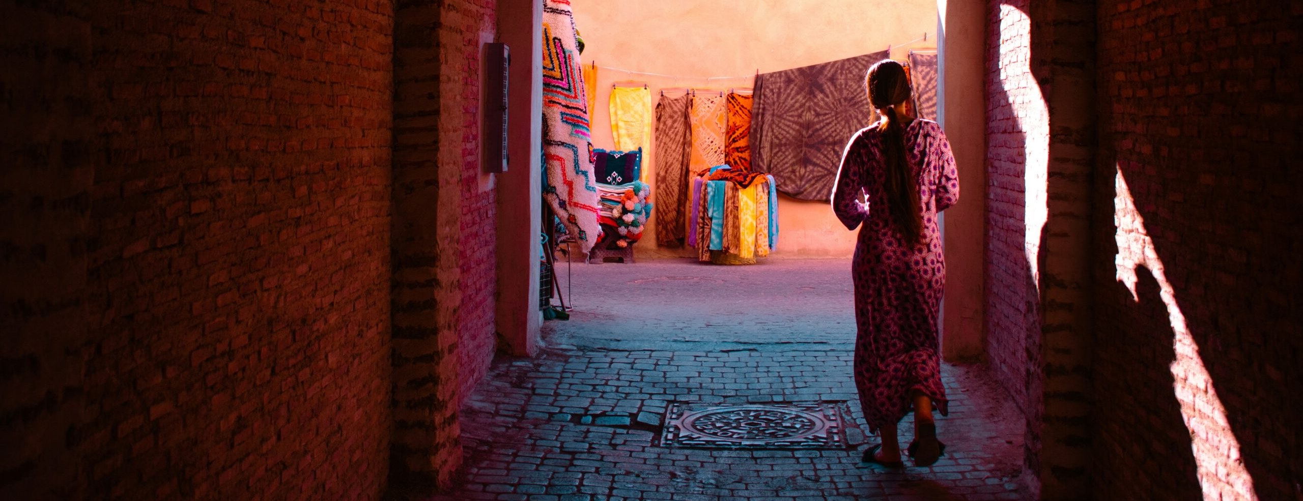 Vrouw wandelt door een poort naar een kleurrijk tapijtwinkeltje in de medina van Marrakech